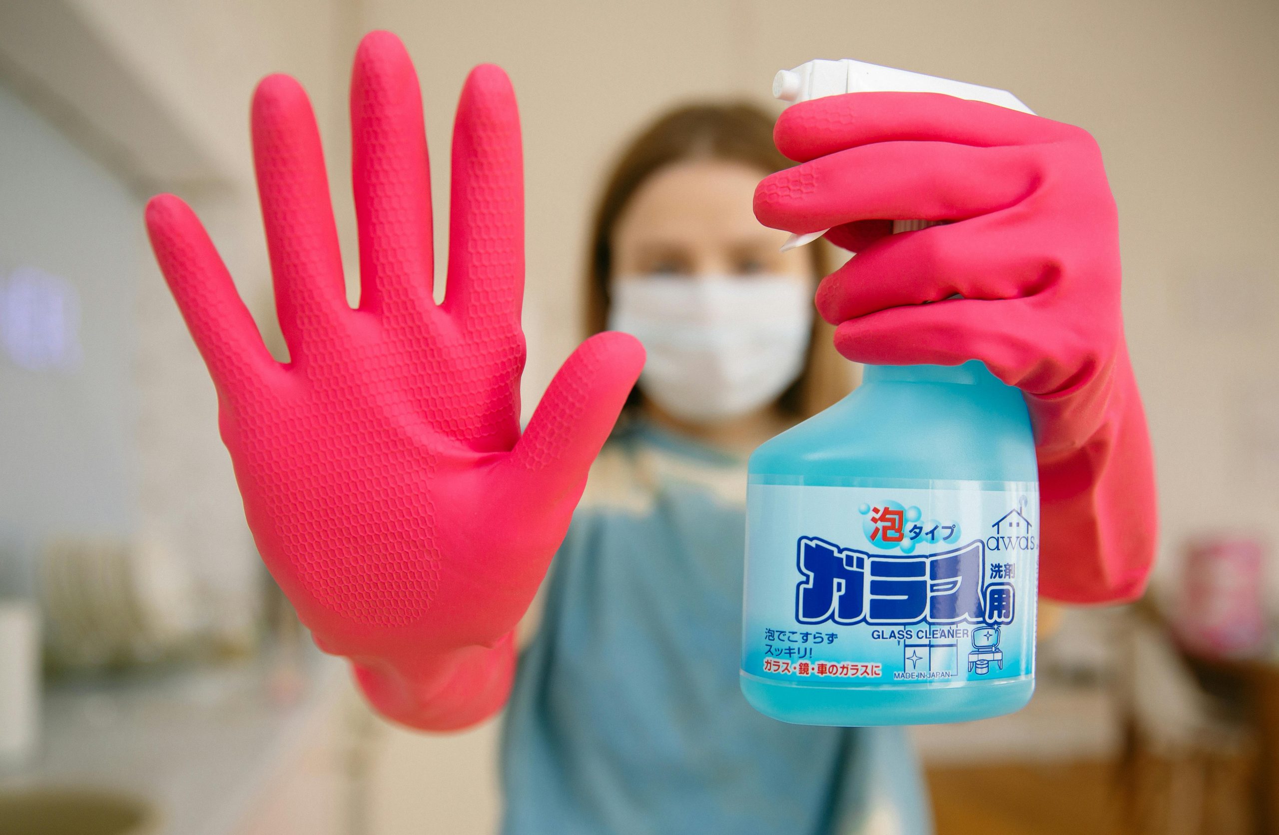 a women with cleaning gloves, mask, and a bottle of cleaning solution